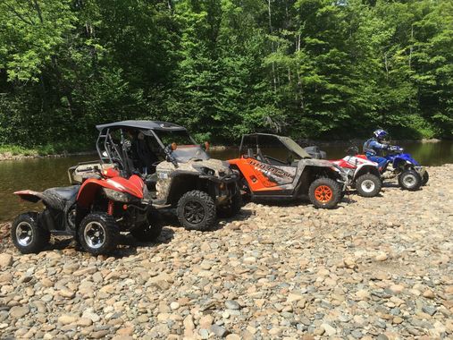 A group of four atvs are parked on a rocky path next to a river.