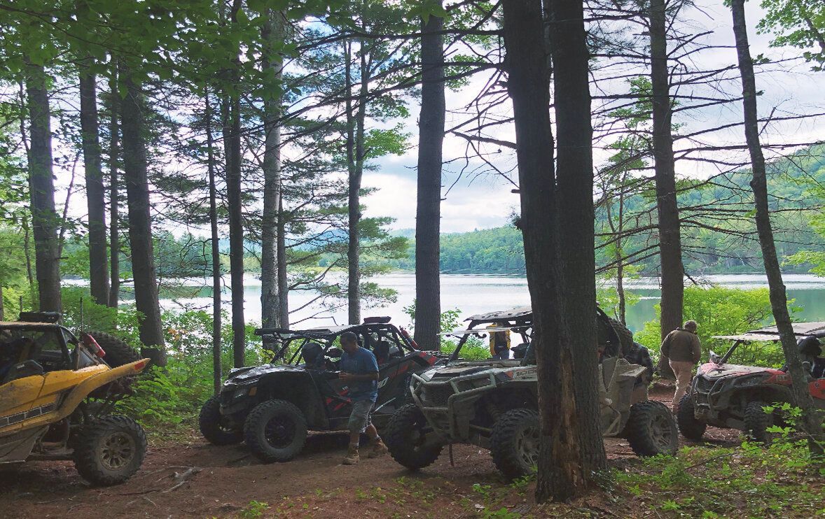 A group of atvs are parked in the woods near a lake