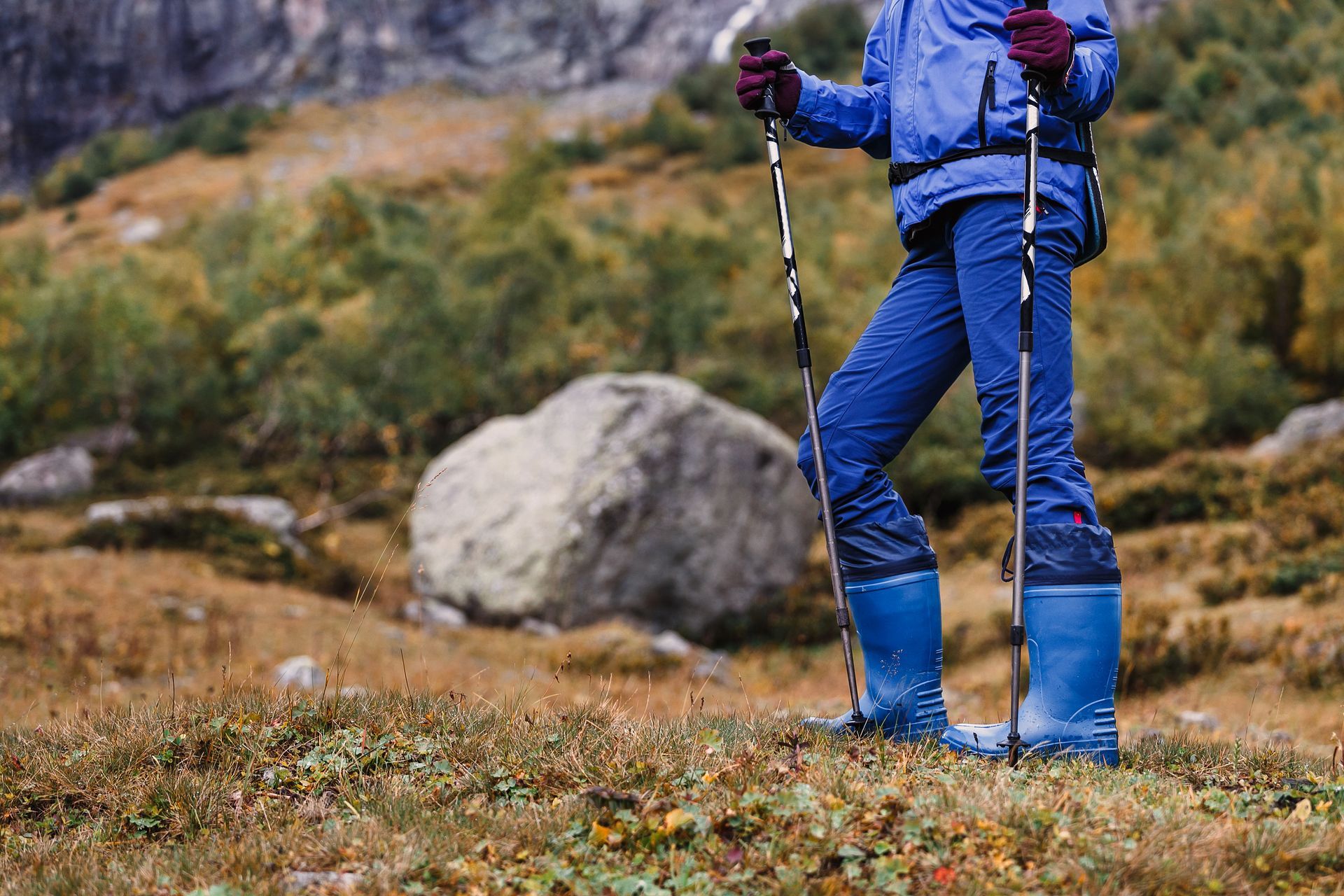 A woman is standing in a field with hiking poles.