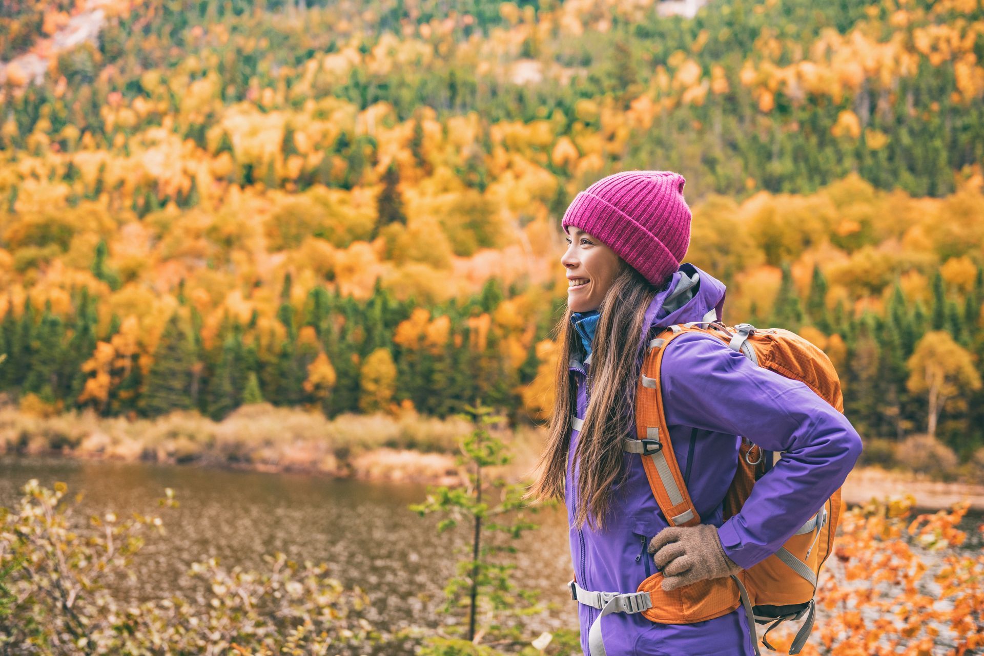 A woman with a backpack is standing in the woods near a lake.