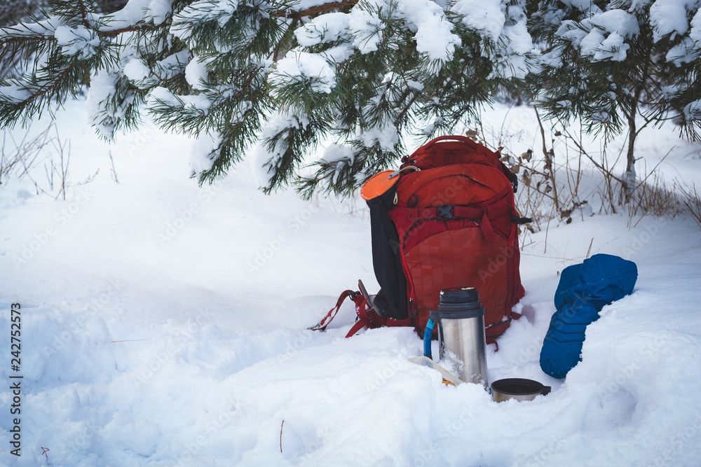 A backpack and a thermos are sitting in the snow.