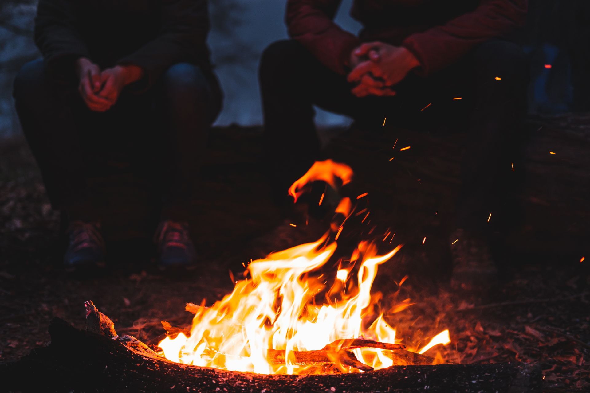 Two people are sitting around a campfire at night.