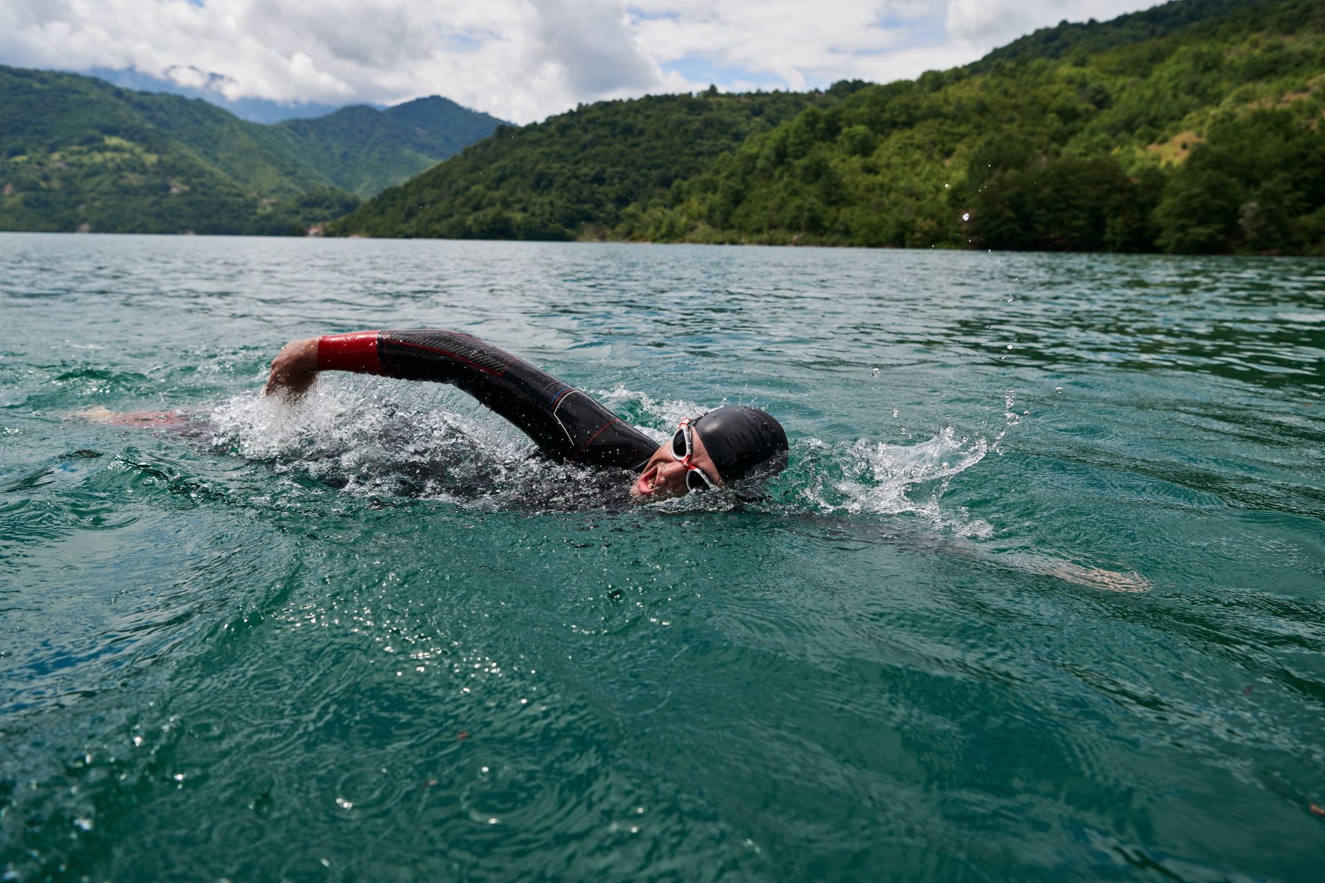 A person is swimming in a lake with mountains in the background.