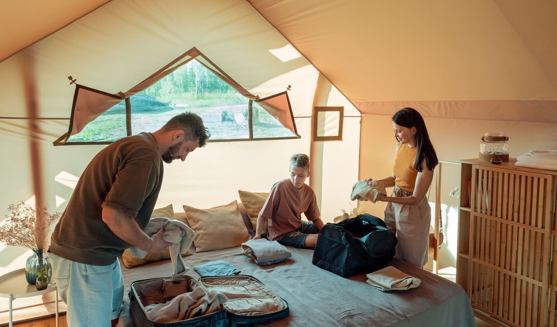 A man and a woman are packing a suitcase in a glamping tent.