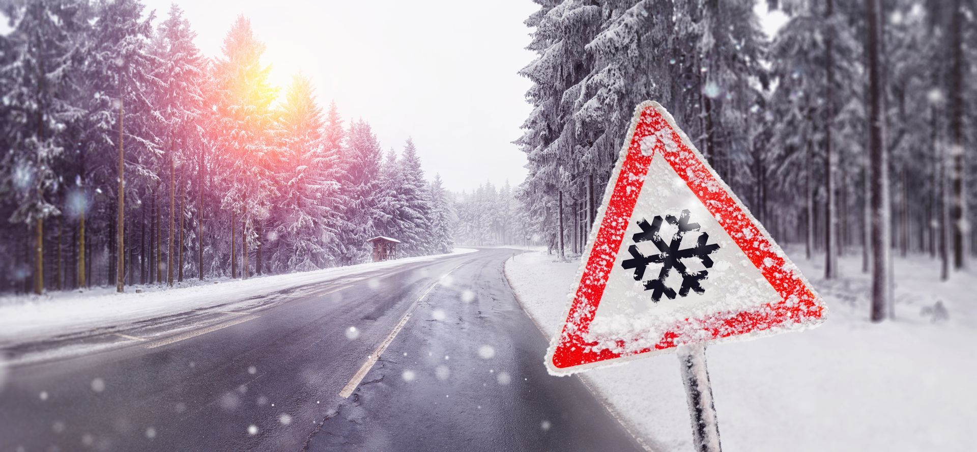 A snowy road with a snowflake sign on the side of it.