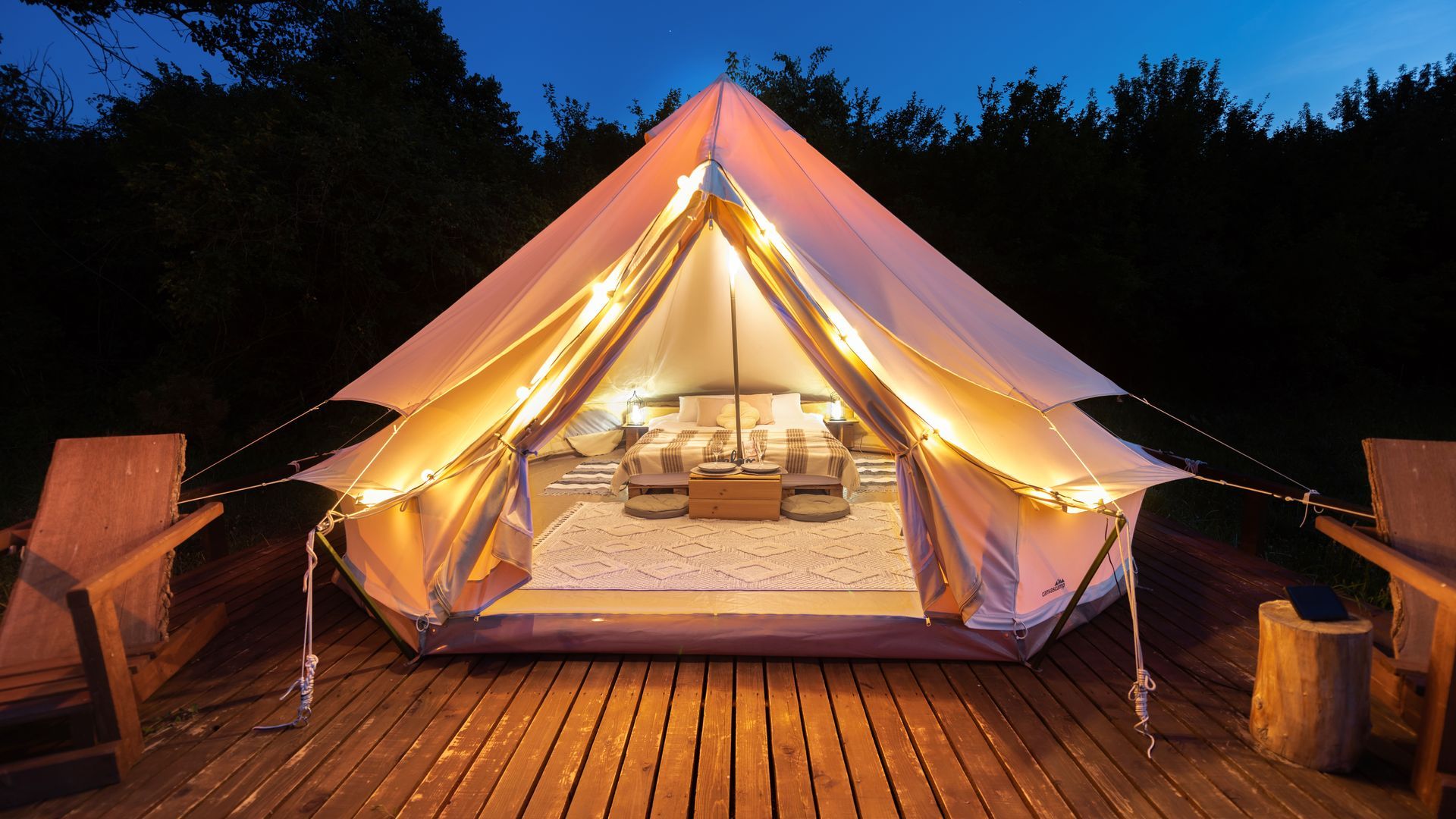 A tent is lit up and sitting on a wooden deck.