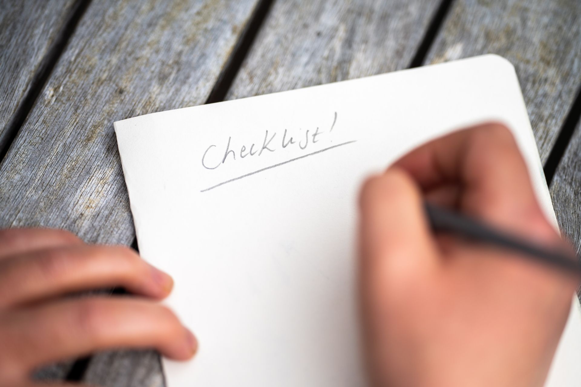 A person is holding a piece of paper that says checklist on it