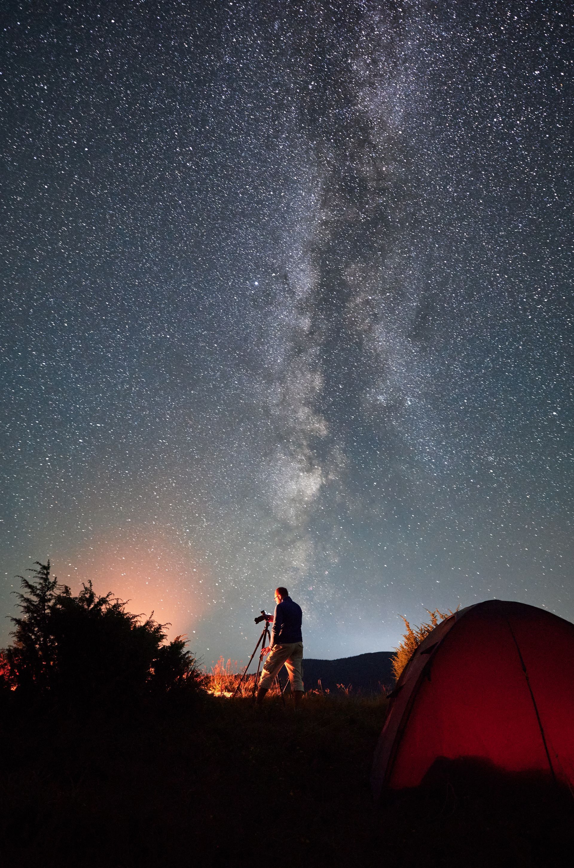 A man is standing in front of a tent under a starry night sky.