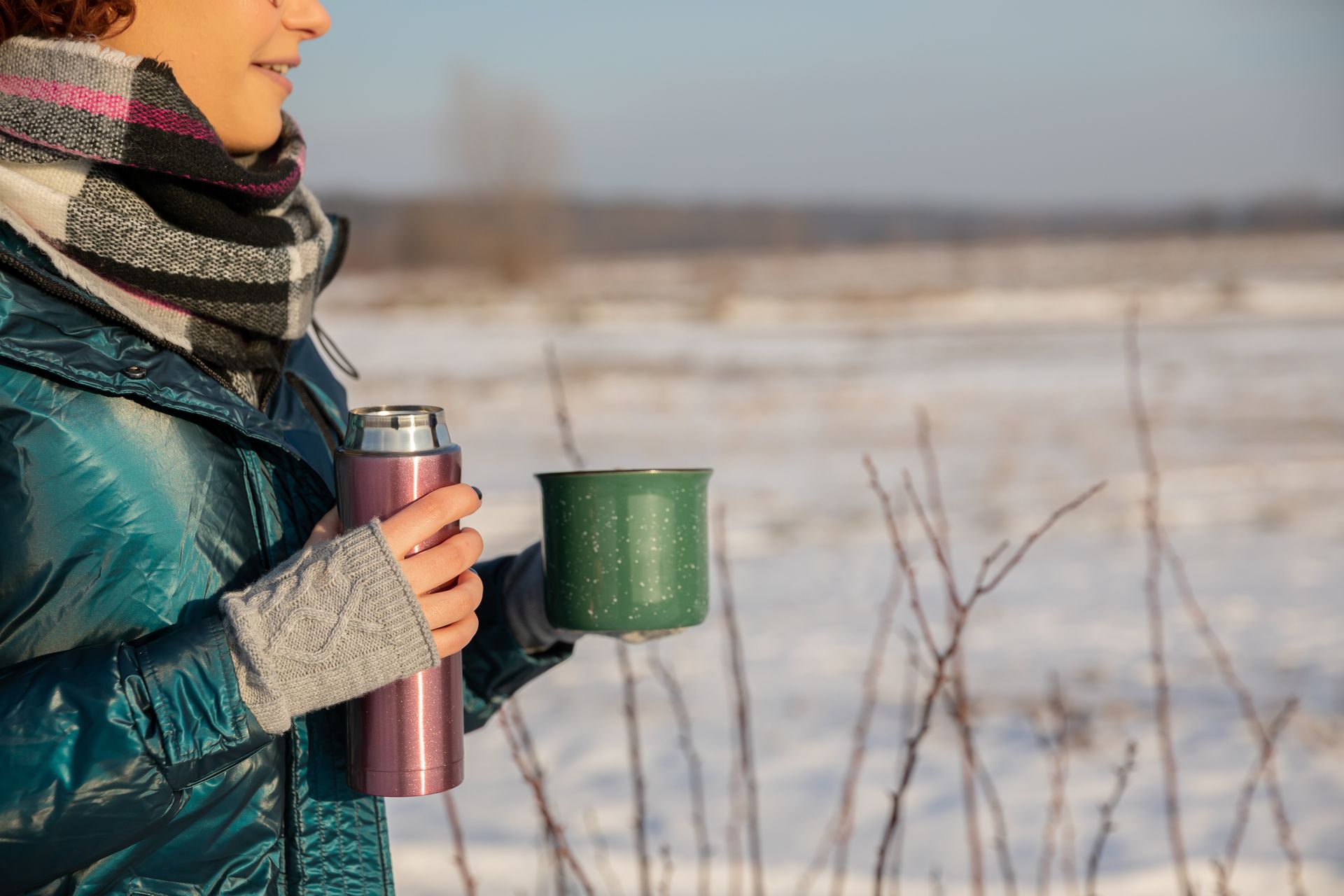 A woman is holding a thermos and a cup of coffee in the snow.