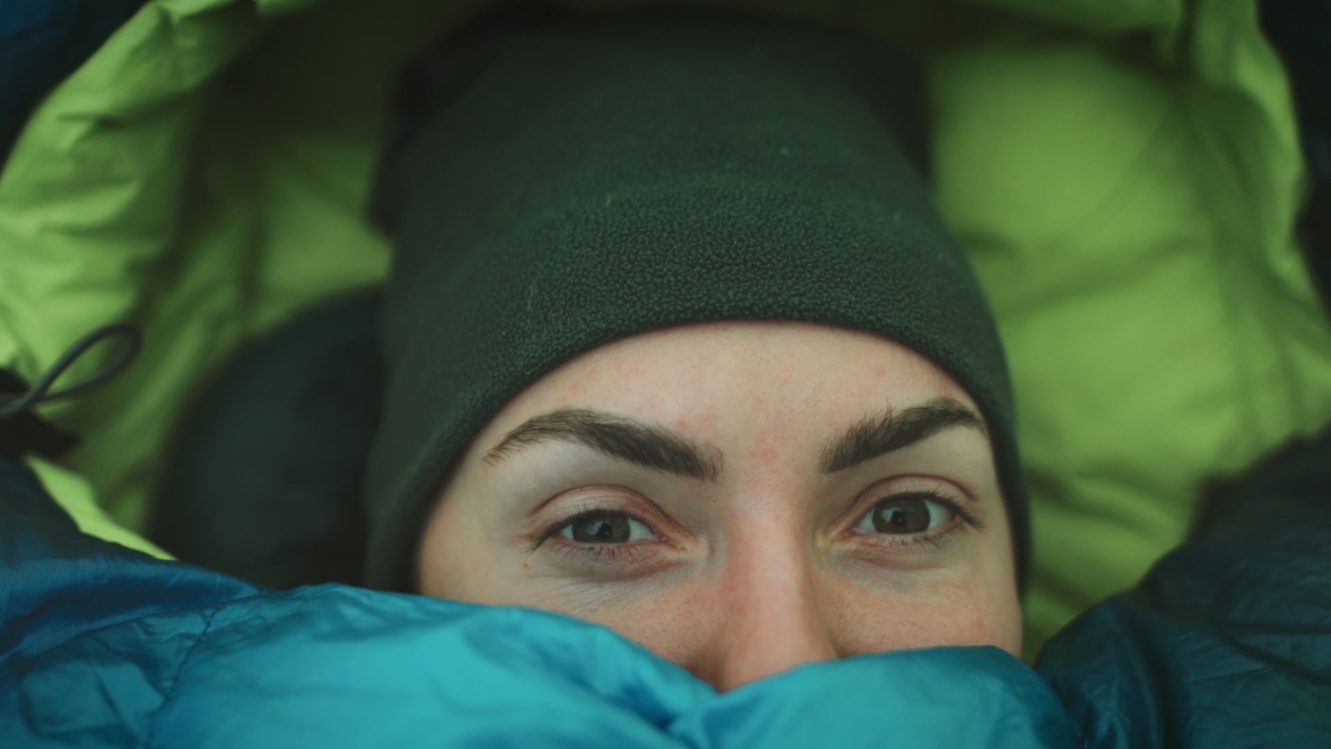 A woman is laying in a sleeping bag with her face covered.