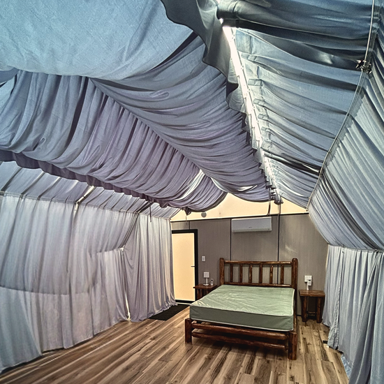 Bed with mosquito net draped overhead in a small room with wood floor and gray curtains