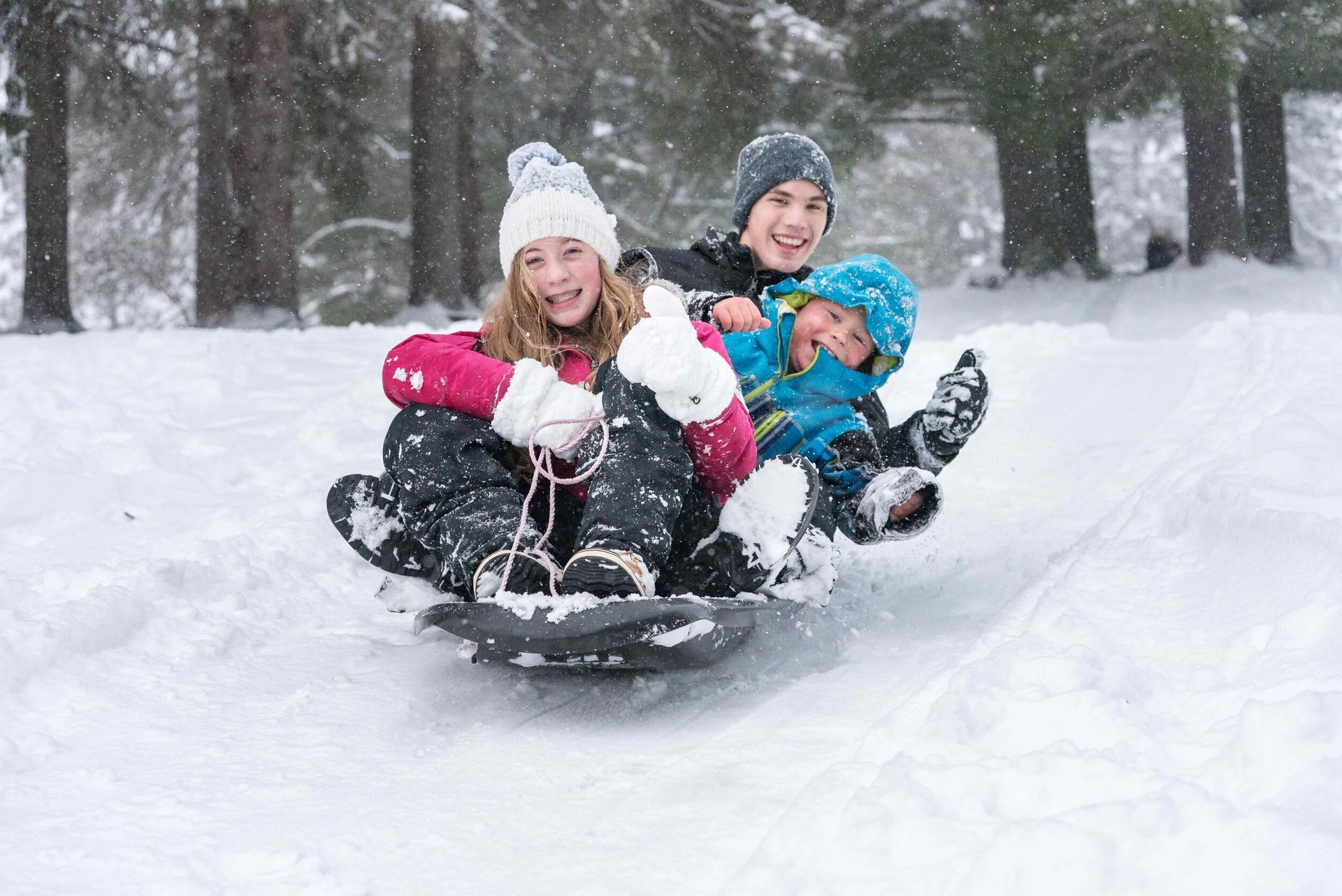 A group of children are sledding down a snow covered hill.