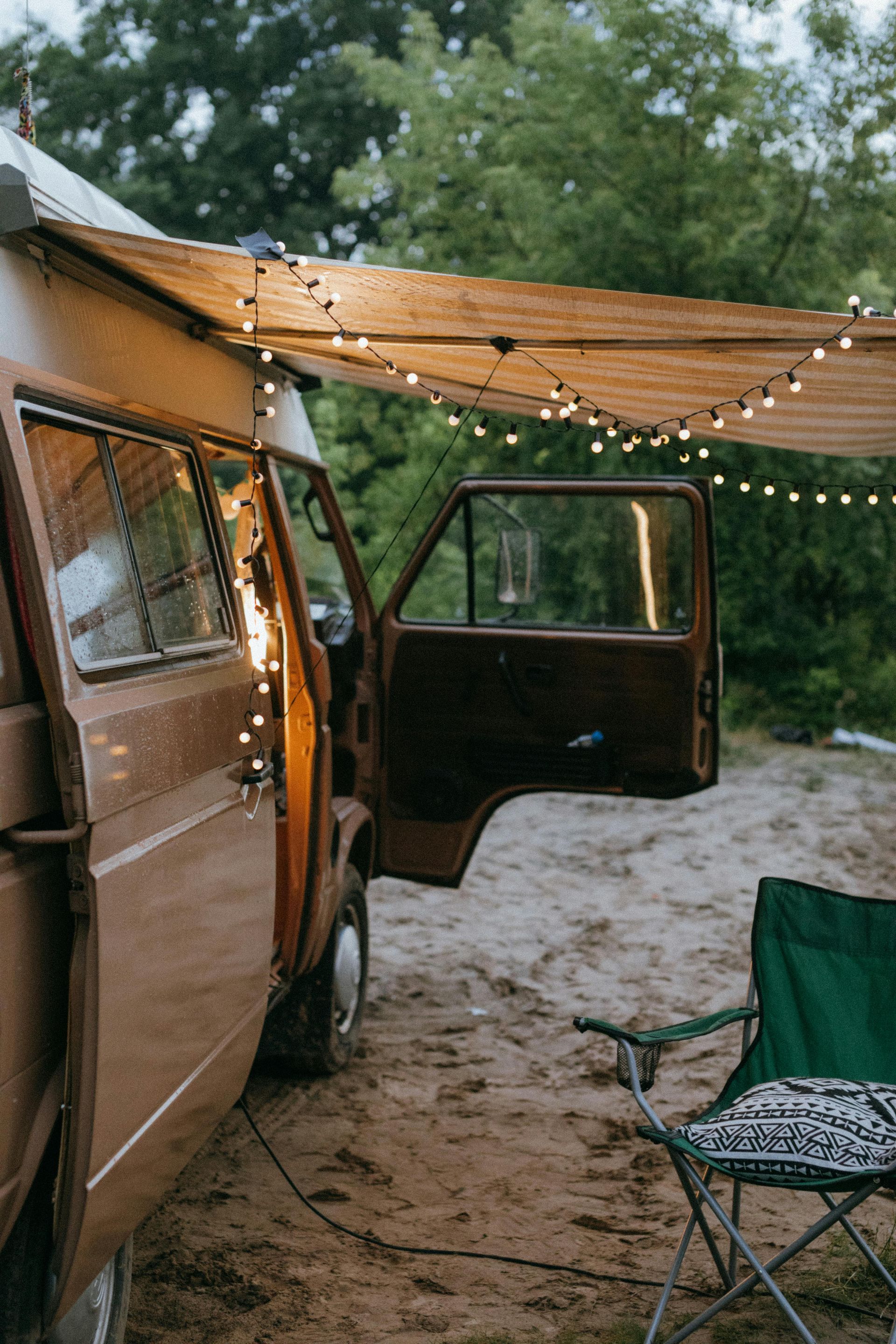 A camper van is parked in the dirt with its doors open and a chair.