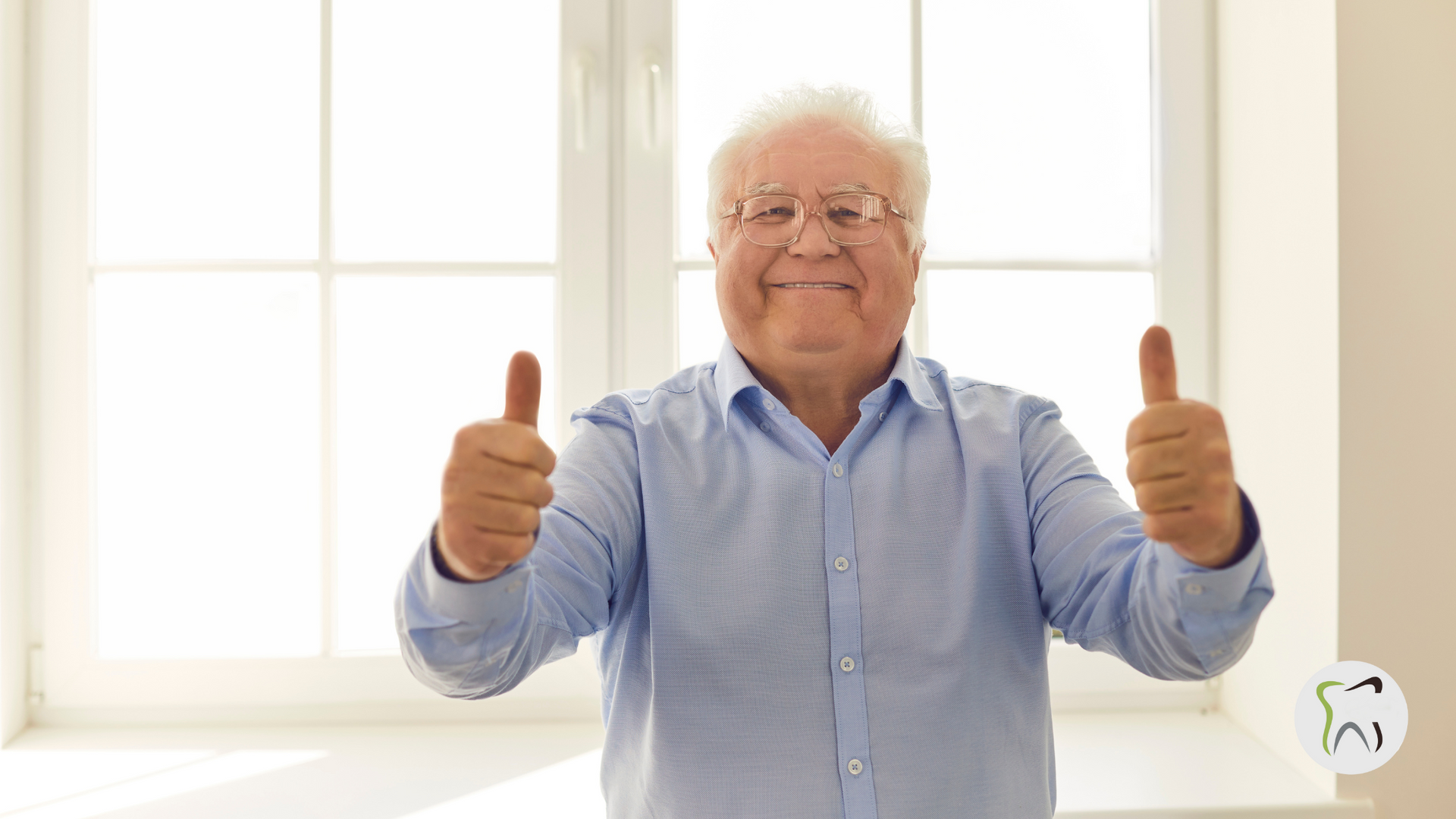 An elderly man is giving two thumbs up in front of a window.