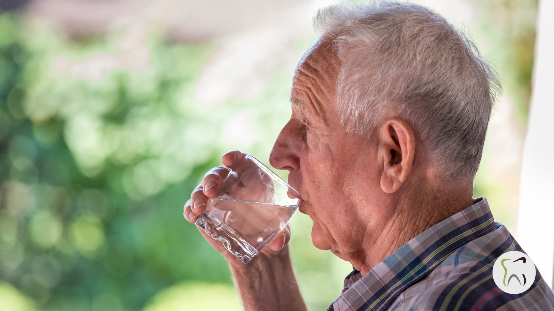 An elderly man is drinking a glass of water.