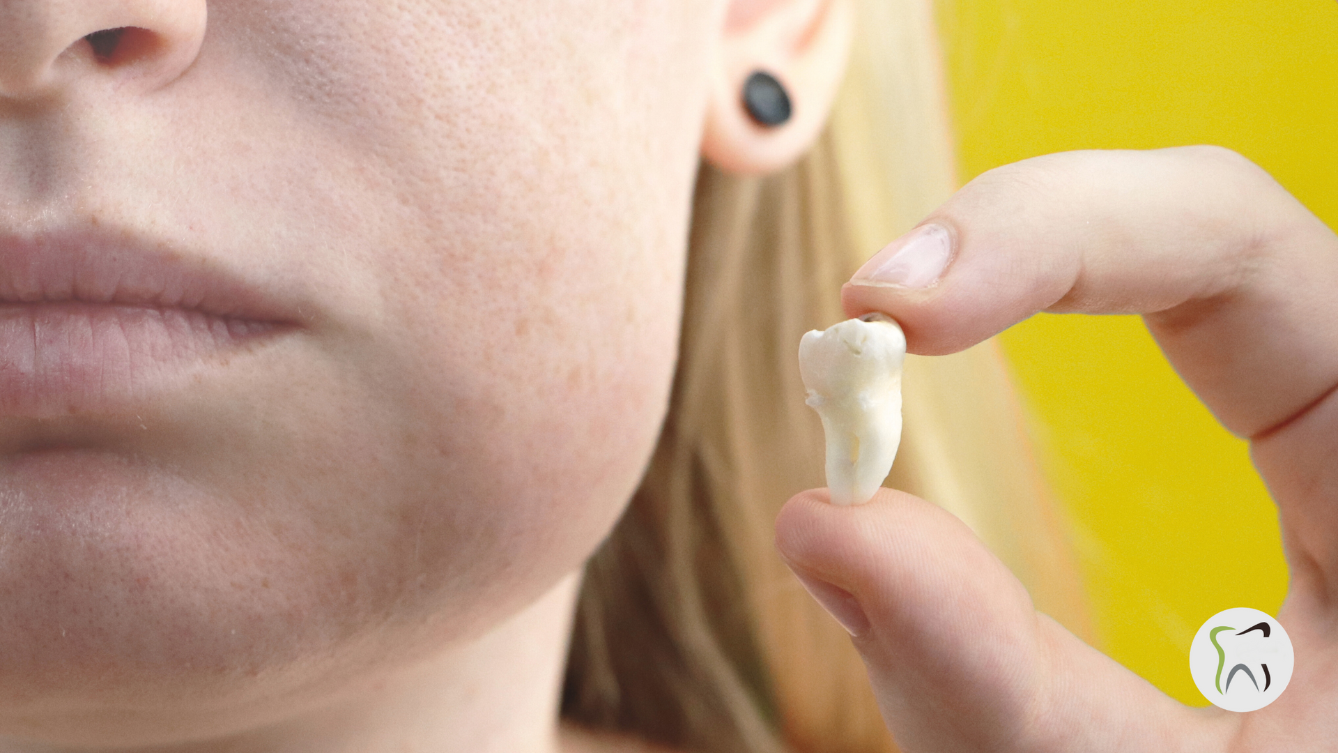 A woman is holding a tooth in her hand in front of her face.