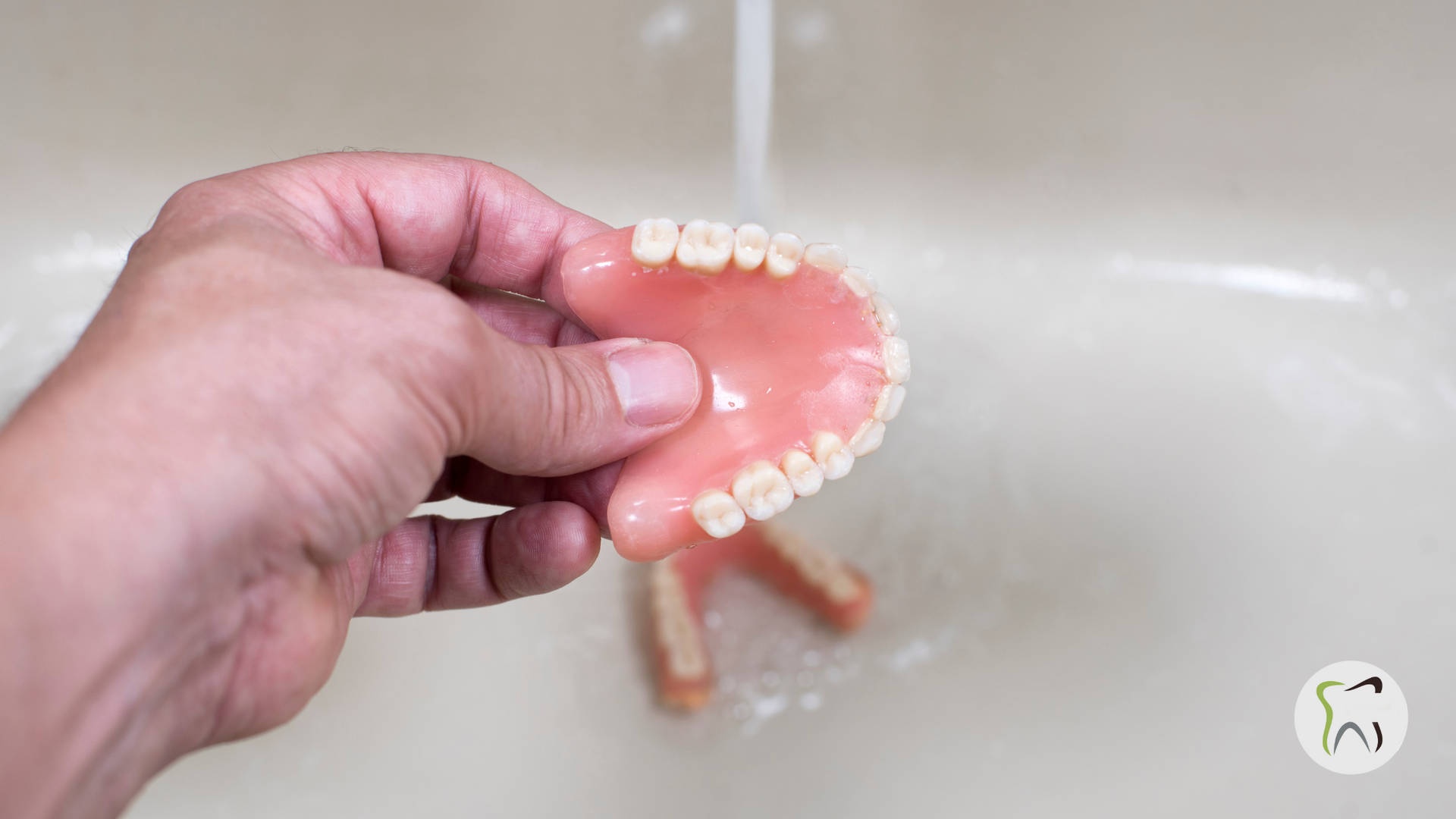 A person is washing a denture in a sink.