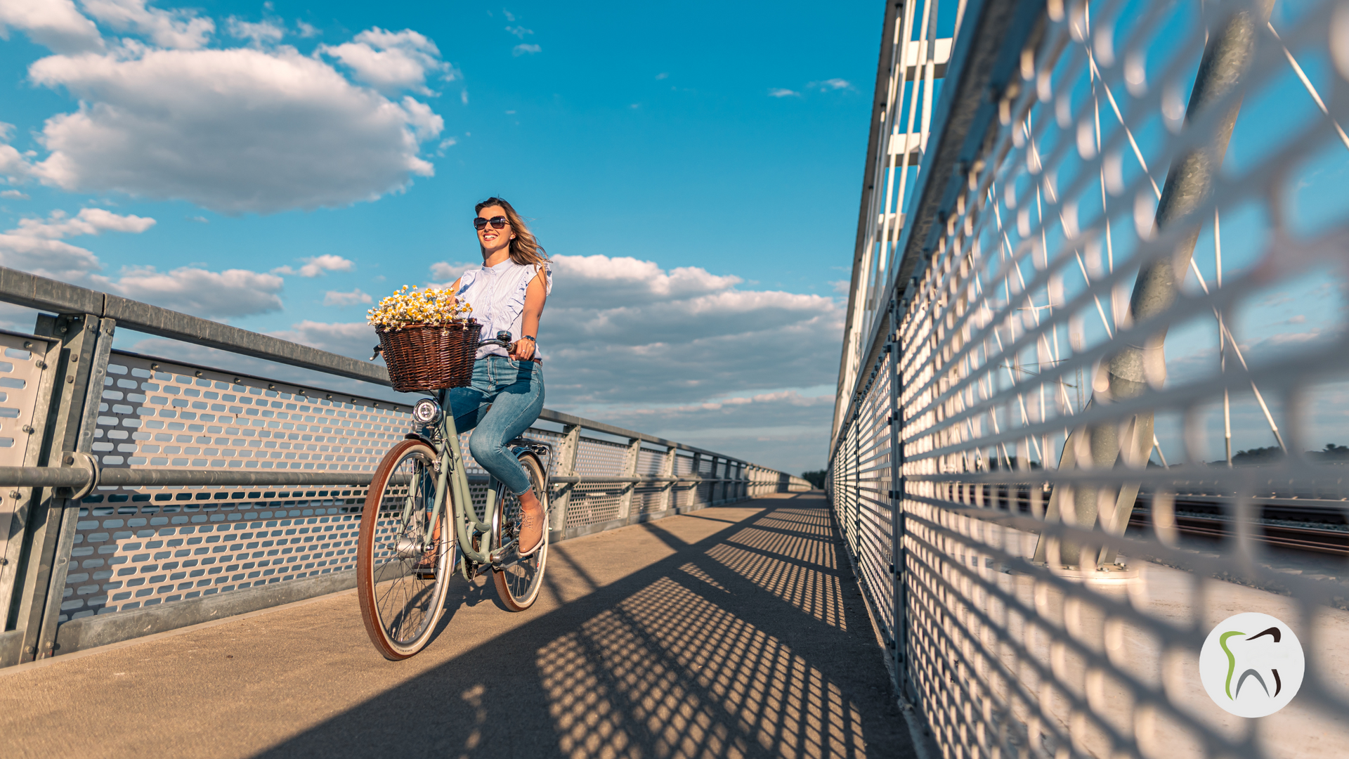 A woman is riding a bike on a bridge with a basket of flowers.