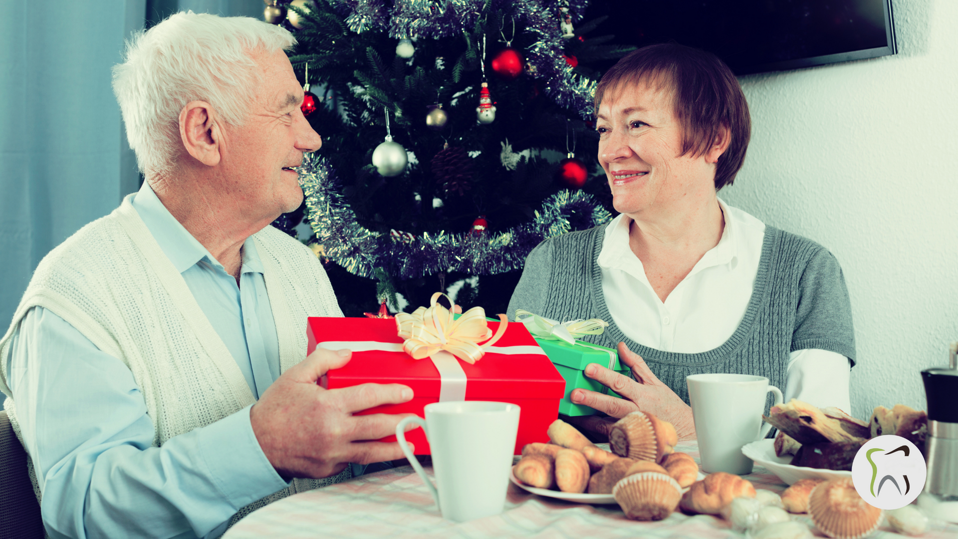 An elderly couple is sitting at a table with a christmas tree in the background.