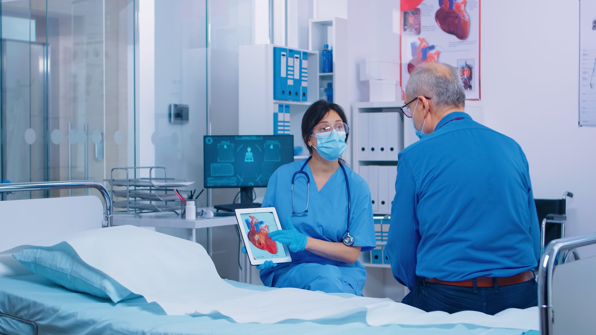 Doctor in scrubs showing heart diagram on tablet to patient in hospital room. Doctor in scrubs showing heart diagram on tablet to patient in hospital room.
