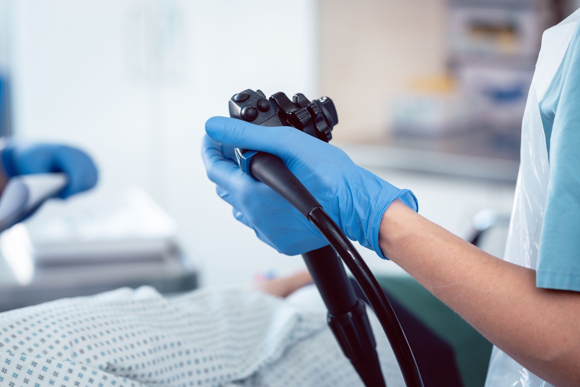 Medical professional in blue gloves holding an endoscope over a patient in a medical setting.