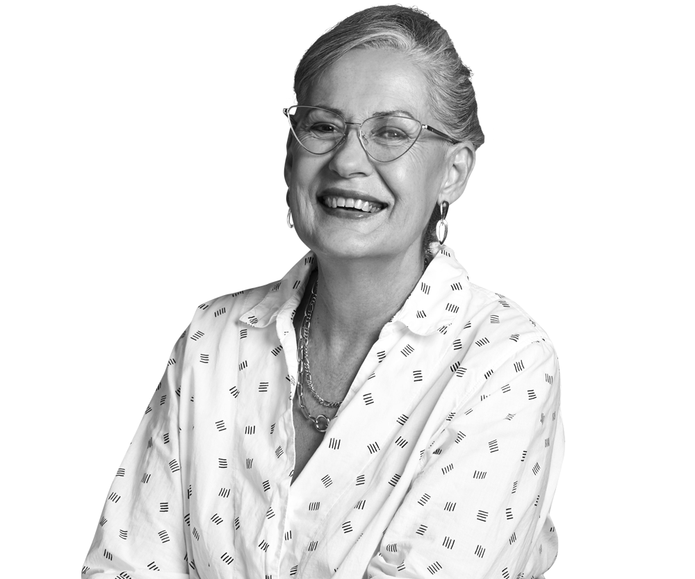 Woman with glasses smiles; wearing a printed blouse and necklace. Woman with glasses smiles; wearing a printed blouse and necklace.