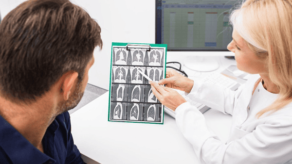 Doctor pointing at lung x-ray, explaining results to patient in an office.