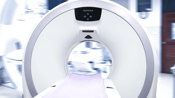CT scanner, white with a purple examination table; blurred interior of a medical facility.