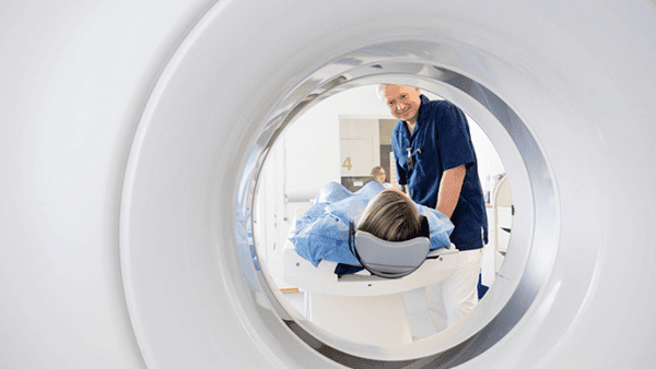 Patient lying on a CT scanner table, attended by a smiling medical professional in a hospital setting.