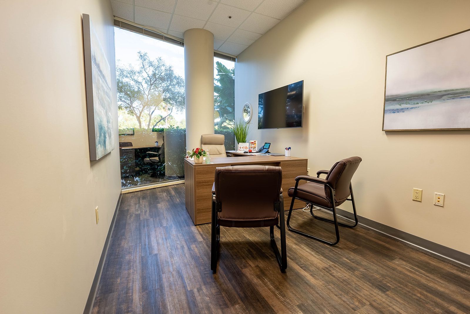 Office with desk, chairs, large window, artwork, and a mounted TV.