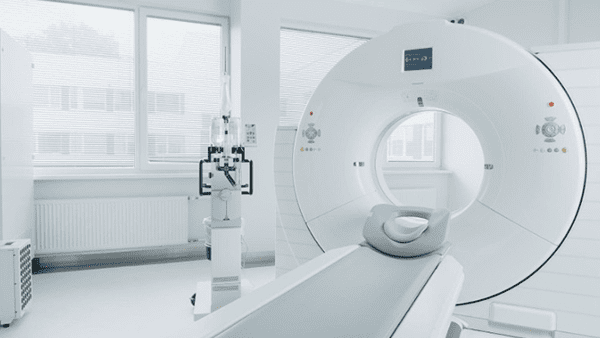CT scan machine in a bright, modern room. A bed is positioned to enter the machine's circular opening.
