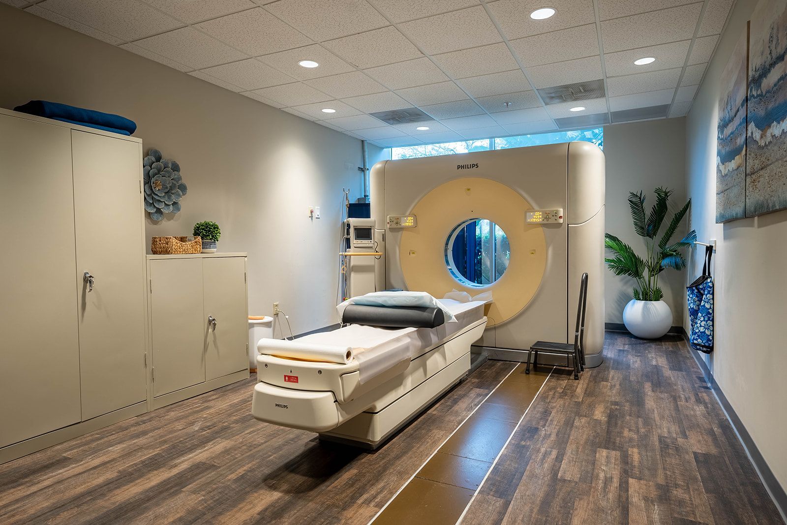 CT scan machine in a medical examination room, with a patient bed and storage cabinets. CT scan machine in a medical examination room, with a patient bed and storage cabinets.