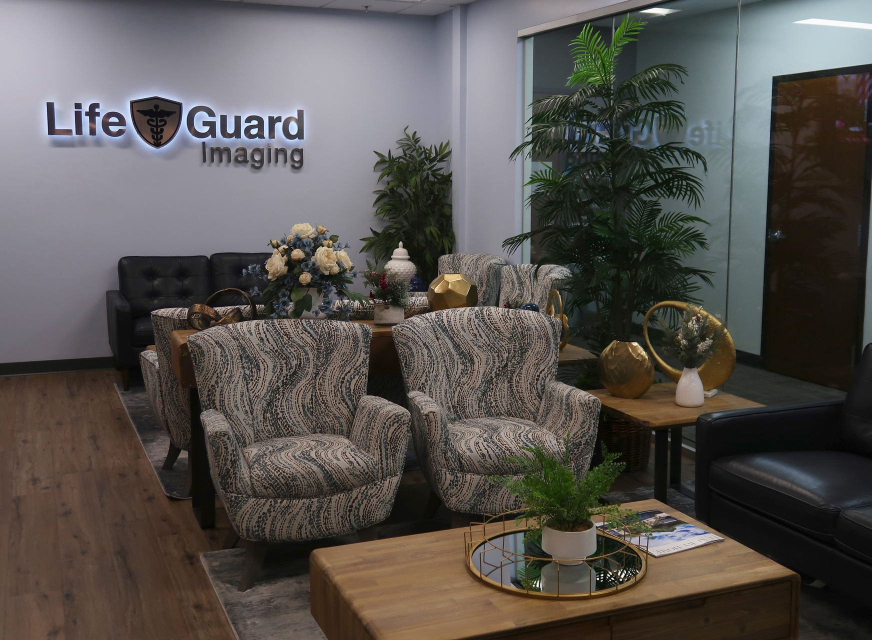Two blue armchairs in waiting area with art and rug; a plant in a white pot, and a brown door.