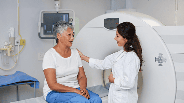 Doctor comforts patient sitting on a medical bed near a CT scanner.