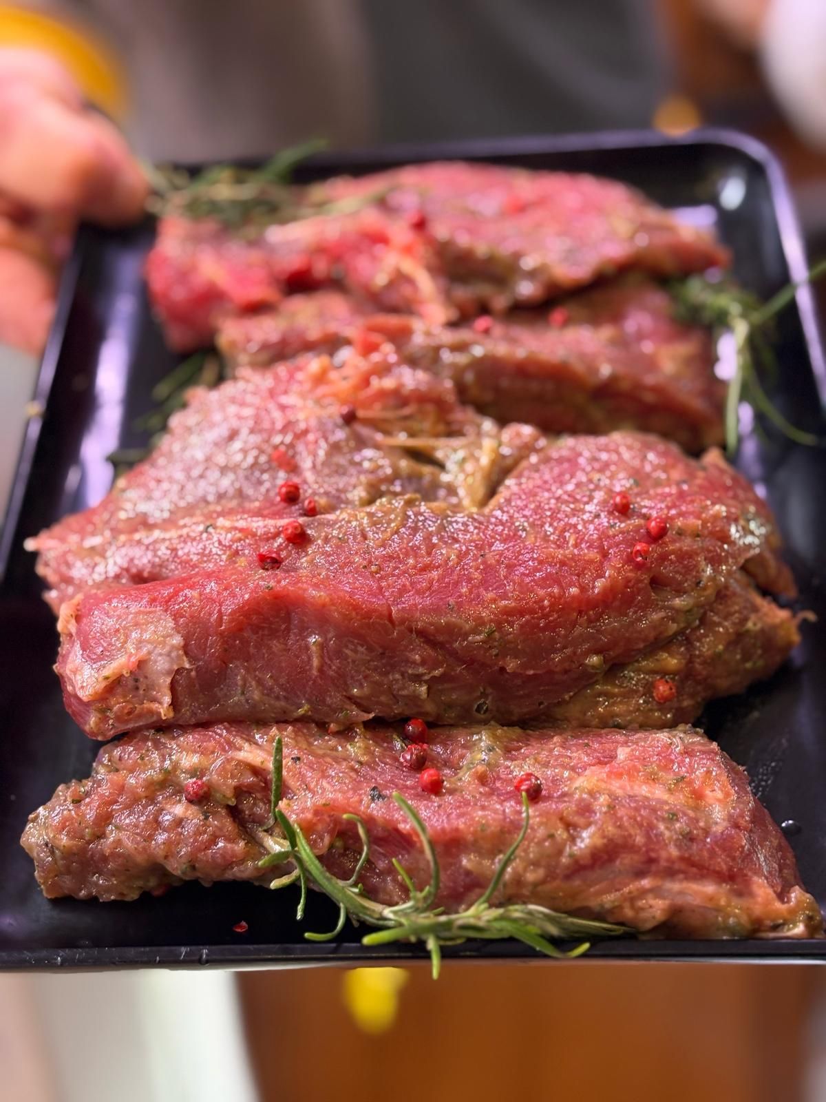 Una persona tiene in mano un vassoio di carne cruda con grani di pepe rosa.
