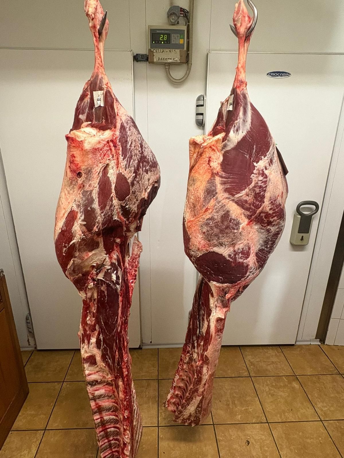 Due pezzi di carne sono appesi a dei ganci in una stanza.