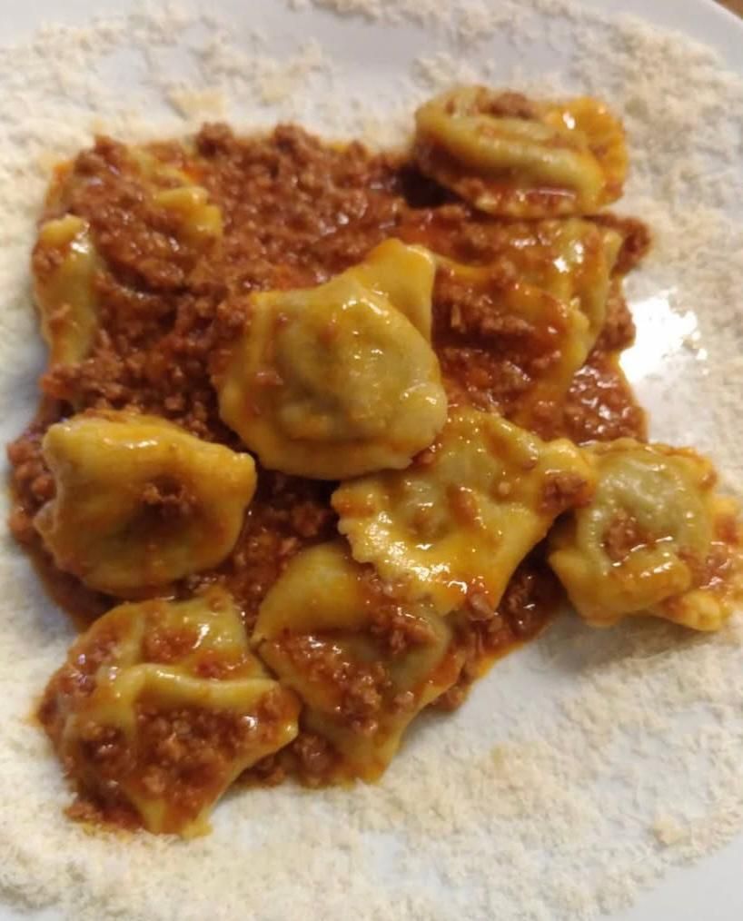 Un piatto bianco condito con ravioli e sugo di carne