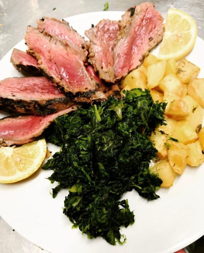 Un piatto bianco condito con carne, patate e spinaci