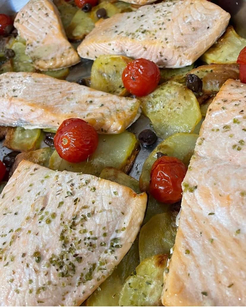 Un primo piano di un piatto di cibo con salmone, patate e pomodori.