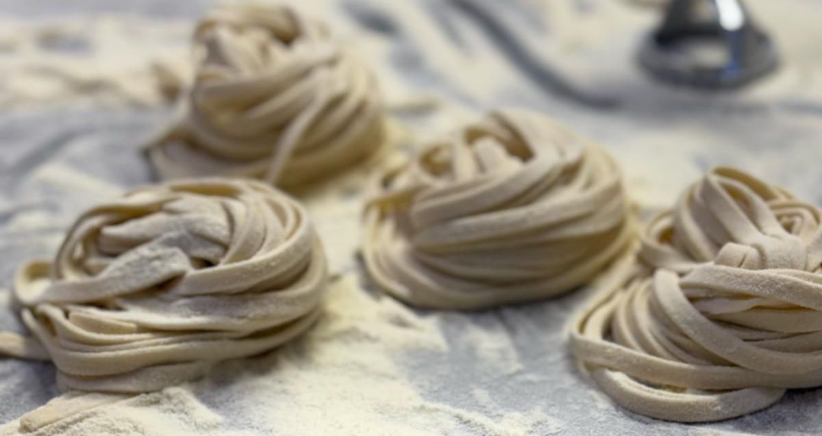 Quattro tagliatelle sono appoggiate su un tavolo ricoperto di farina