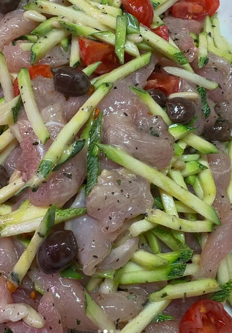 Un primo piano di un'insalata con carne, zucchine, olive e pomodori.