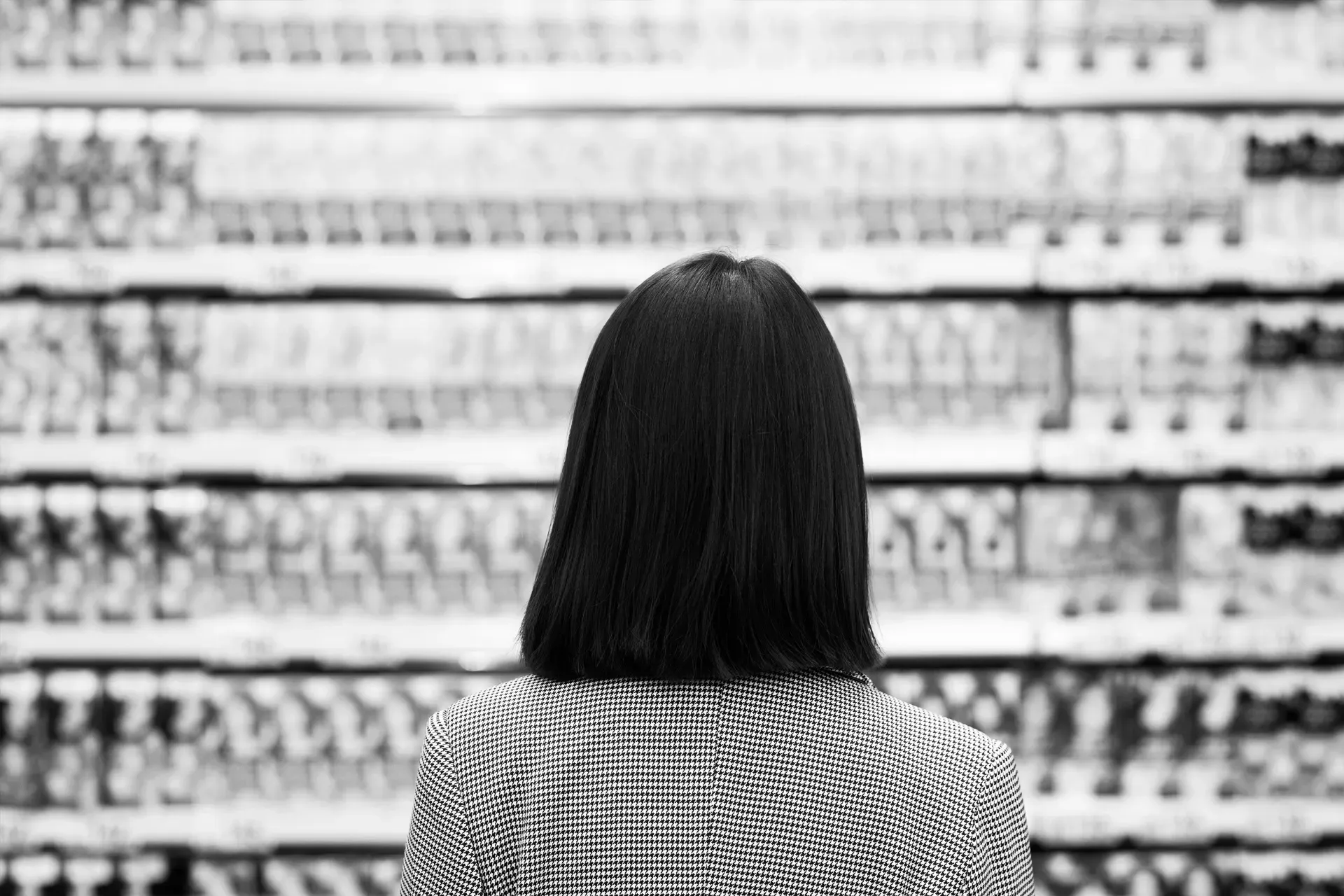 Person with dark hair and patterned jacket facing a grocery store shelf, back to the viewer.