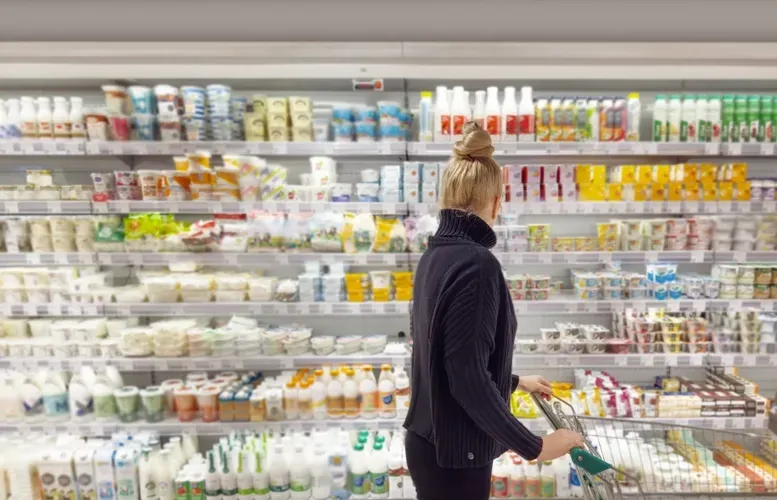 Woman shopping in refrigerated dairy aisle, reaching for a product.
