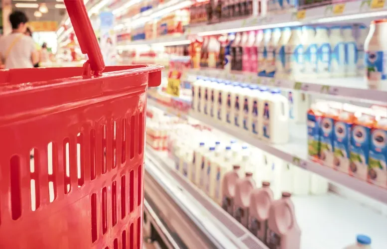 Red shopping basket in a grocery store aisle with dairy products.