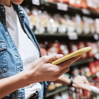 Person using a phone in a grocery store, browsing shelves while holding a shopping cart.
