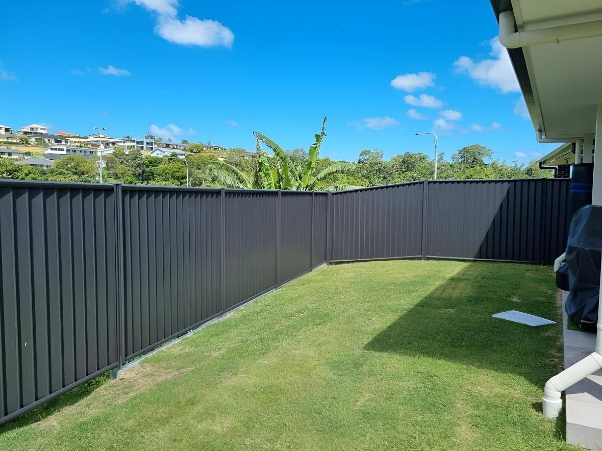 A Black Fence Surrounds a Lush Green Yard — Quality Fencing Solutions in Ballina, NSW
