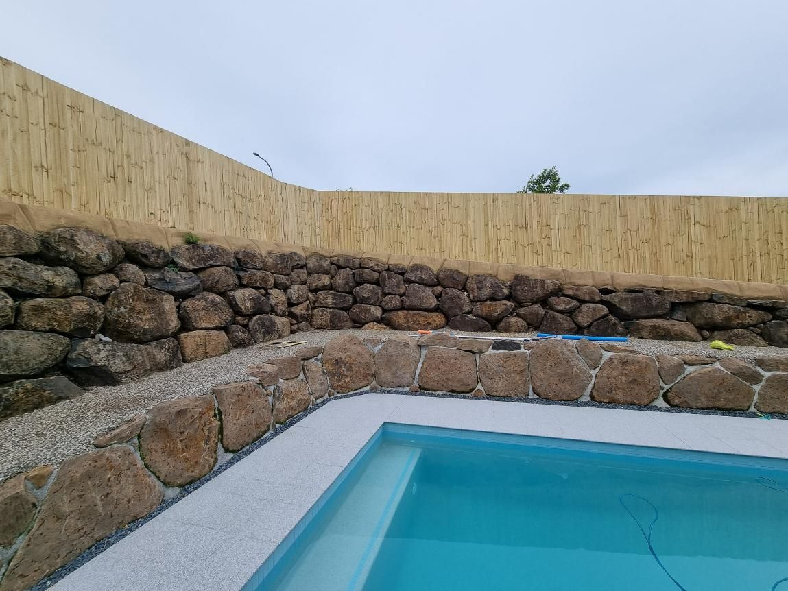 A Swimming Pool Surrounded by Rocks and A Wooden Fence — Quality Fencing Solutions in Ballina, NSW