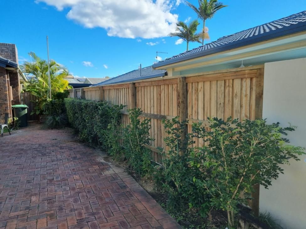 A Wooden Fence Surrounds a Brick Driveway in Front of A House — Quality Fencing Solutions in Ballina, NSW