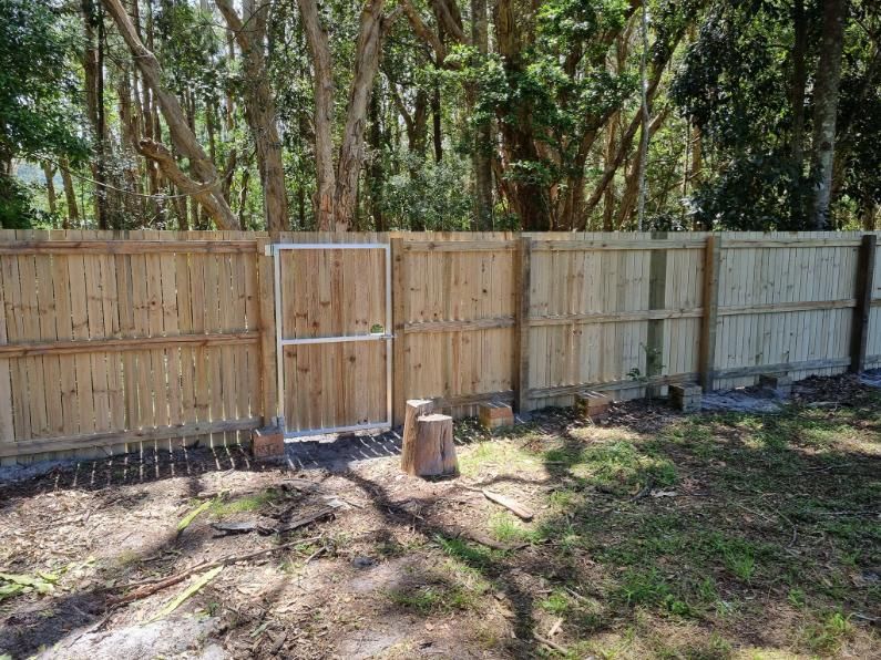 A Wooden Fence with A Gate in The Middle of A Yard Surrounded by Trees — Quality Fencing Solutions in Ballina, NSW