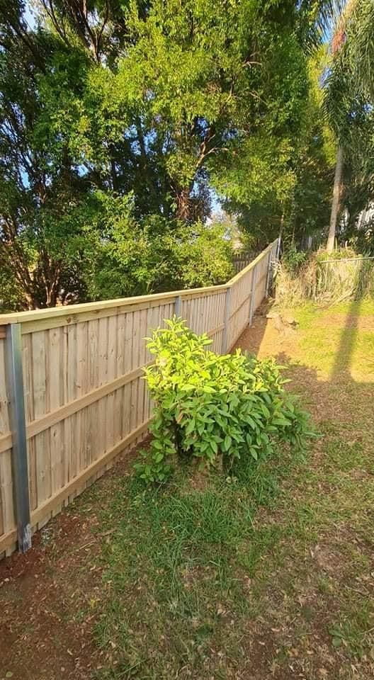 A Wooden Fence Is Surrounded by Trees in A Backyard — Quality Fencing Solutions in Ballina, NSW